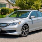 Srebrna Honda Accord zaparkowana przy ulicy, na tle domów i zielonych żywopłotów